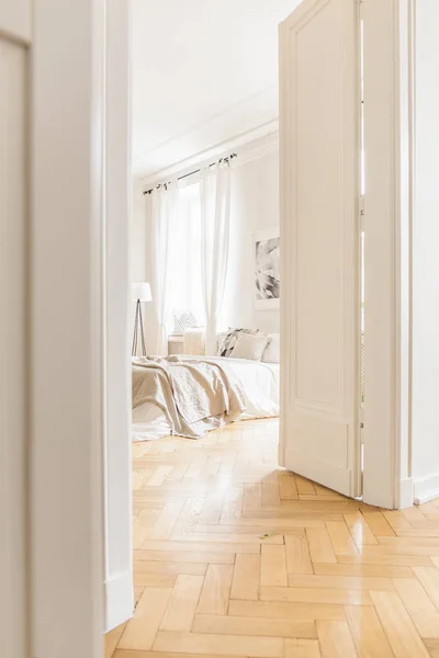 シンプルなデザインとヘリンボーン フローリング スタイリッシュで明るい寝室のインテリアに背の高い オープンの白いドアを通ってを表示します — ストック写真