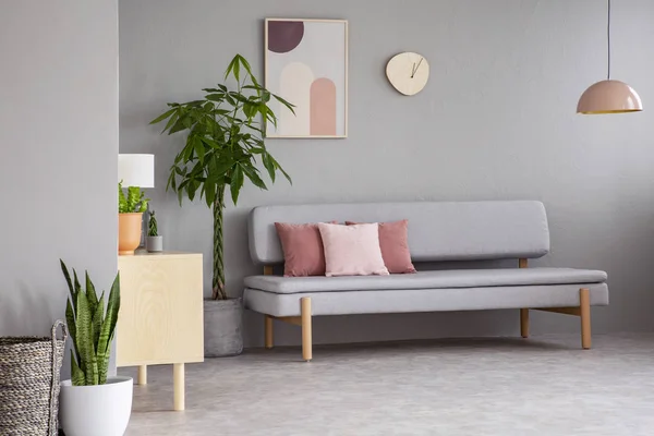 海报和时钟以上灰色沙发在公寓内部与植物和粉红色的灯 真实照片 — 图库照片