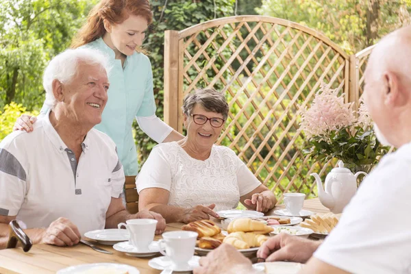 Happy senior couple eating breakfast and a nurse taking care of them in the garden