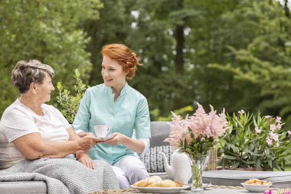 快乐的护士给老妇人喝茶 同时在阳台上吃早餐 — 图库照片