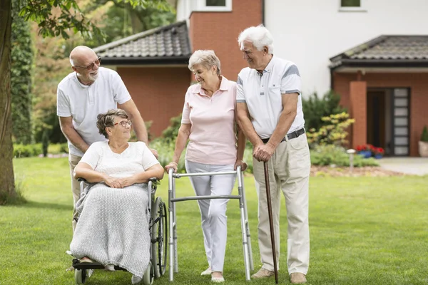 Disabled elderly woman in a wheelchair and happy friends in the garden