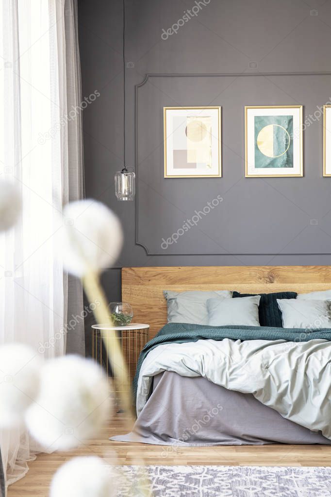 Double bed with wooden headboard, pillows and bright sheets standing in grey bedroom interior in the photo with blurred foreground