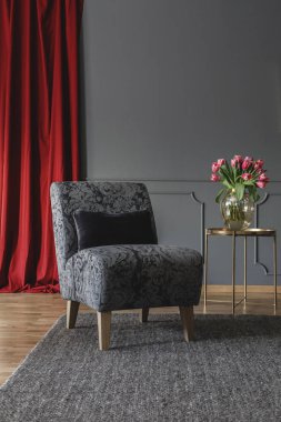 Altın metal masa ve kırmızı perde taze lale ile zarif oda iç karanlık halı üzerinde siyah yastık ayakta gri çiçek sandalyeyle. Grafiğiniz için yer ile boş duvar