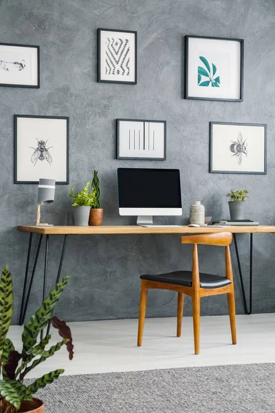 桌面上的海报画廊与台式计算机在灰色家庭办公室内部与椅子 真实照片 — 图库照片