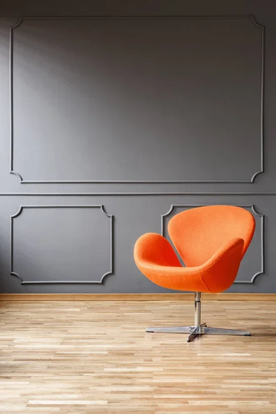 Modern orange armchair in minimal grey living room interior with wooden floor. Real photo with a place for your furniture