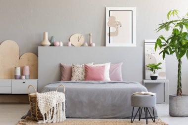 Battaniye ve dışkı gri yatak odası iç palmiye ve poster ile yatakta önünde sepetle. Gerçek fotoğraf