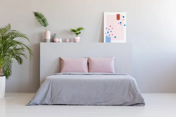 海报和植物在床上的床头与粉红色的垫子在灰色卧室内部 真正的照片与一个地方为您的床头柜 — 图库照片