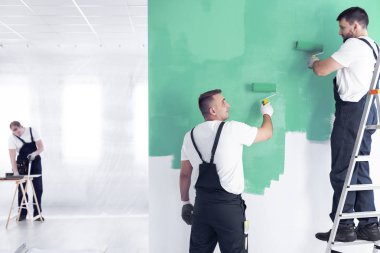 Bir merdiven ve bir yenileme mürettebat işçi silindirler ve geniş ofis iç bulanık bir arka planda bir marangoz ile yeşil bir duvar boyama duvar ressamı