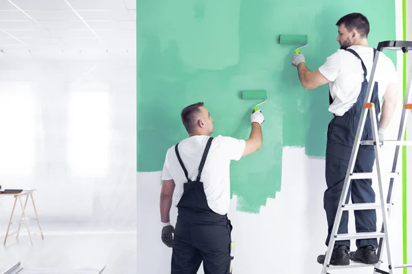 同僚とインテリアを改装している間緑の壁を塗る梯子の上の画家 — ストック写真