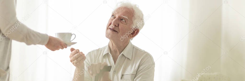 Panorama of happy elderly man with walking stick taking tea