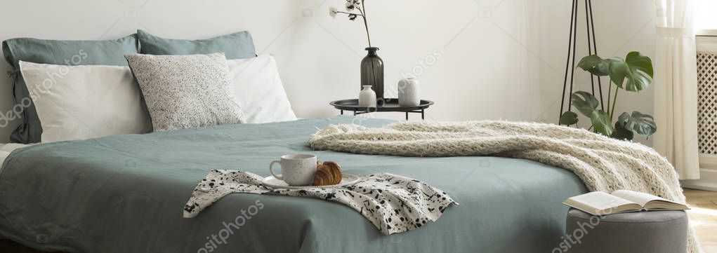 Black metal bedside table with flowers in vase in real photo of bedroom interior with king-size bed with pastel bedclothes, knit blanket and breakfast tray — Stock Image Black Metal Bedside Table Flowers Vase Real Photo Bedroom Interior Stock Picture