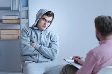 Bir psikolog ve içine kapanık bir sorunlu genç çocuğun kollarını onun göğüs kısmı çarpı işareti ile kapalı pozisyonda oturan arasında ayrı bir tedavi oturum.
