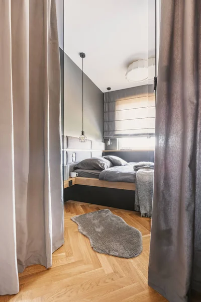 窗帘和毛皮在明亮的卧室内部与灰色床单在木床旁边的窗口 真实照片 — 图库照片