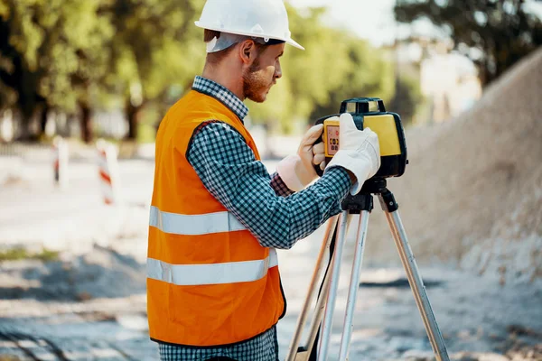 Engineer in reflective vest and white helmet using geodetic equipment