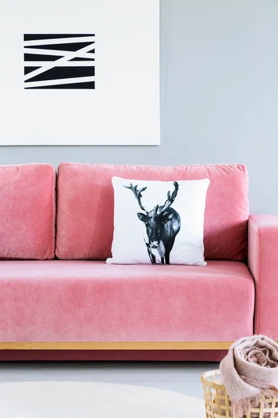 Pillow with deer case placed on pink velvet sofa in the real photo of bright living room interior with modern poster on the wall
