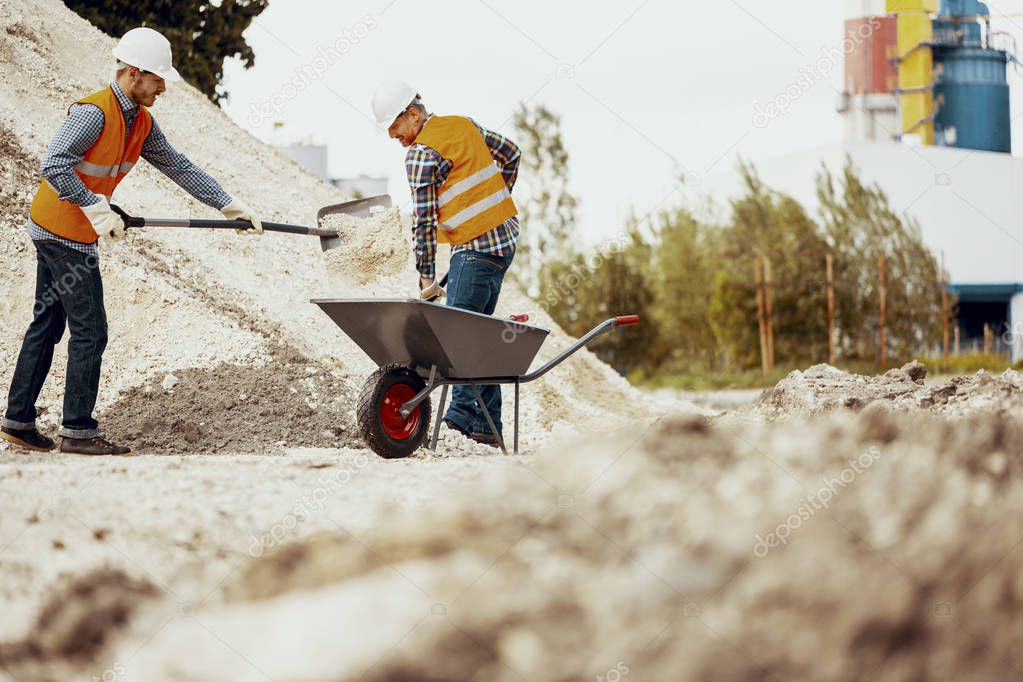 Low angle on workers in reflective vests with shovels and barrow