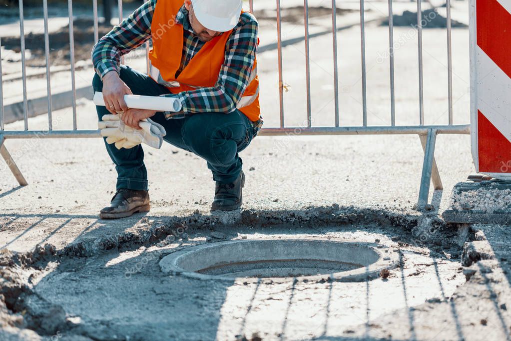Engineer in reflective vest standing near a hole in the road during carriageway work