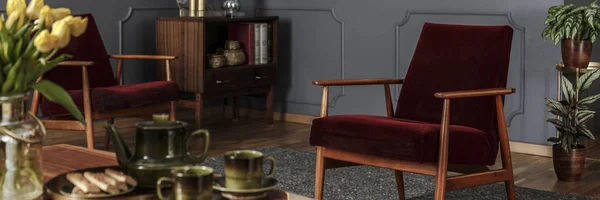 全景的老式勃艮第红色扶手椅与木框架在优雅的灰色客厅内部 真实照片 — 图库照片