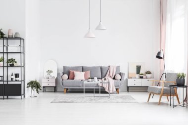 Patterned wooden armchair in white living room interior with pink pillows on grey sofa. Real photo clipart