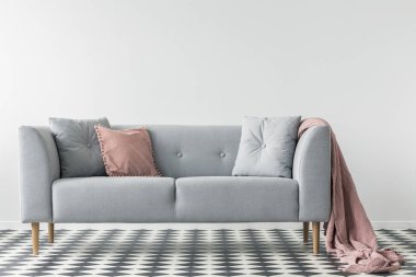 Pembe battaniyeyle yastık beyaz salon iç damalı zemin üzerinde gri kanepede. Gerçek fotoğraf
