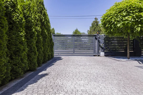 Green trees and grey entry gate to the property during summer. Real photo