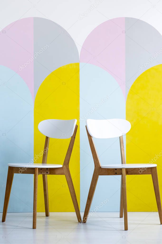 Two chairs set on a patterned wall with yellow accents in bright office interior. Real photo