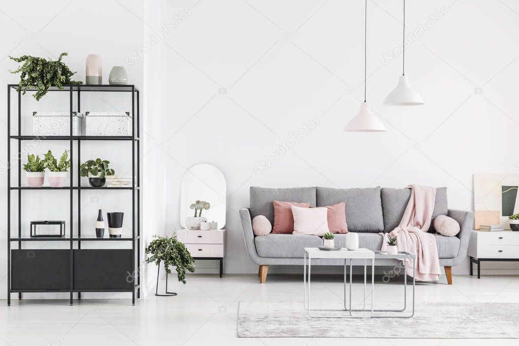Lamps above table in white spacious living room interior with grey sofa with pink blanket. Real photo