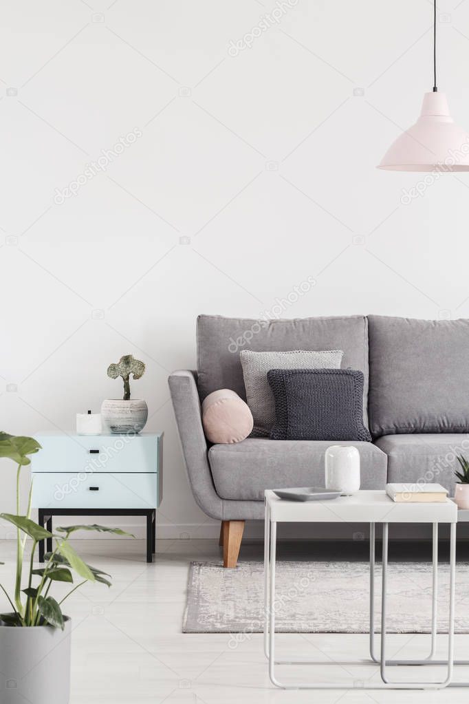 Cropped photo of a sofa next to small cabinet and coffee table in a living room interior. Real photo. Place for your graphic