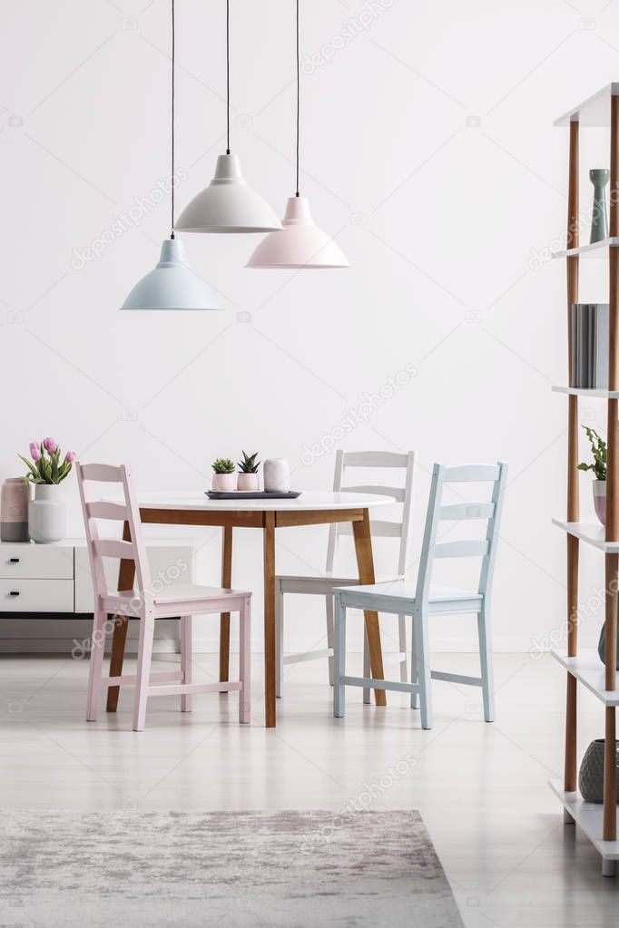 Pastel lamps above table with chairs in white dining room interior with grey carpet. Real photo