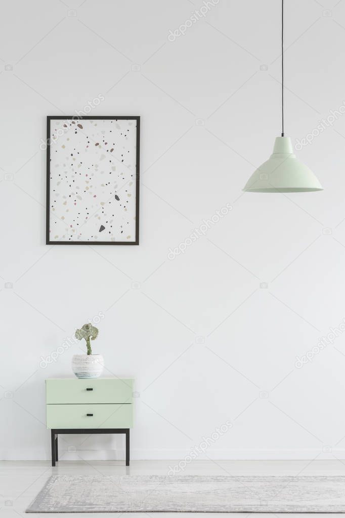 Poster above cabinet with plant in white minimal living room interior with lamp above rug. Real photo with a place for your armchair
