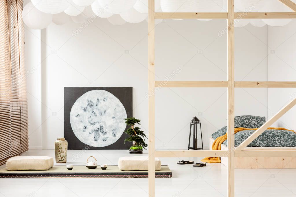 Pillows on the floor and moon poster in bedroom interior with lantern next to wooden bed. Real photo