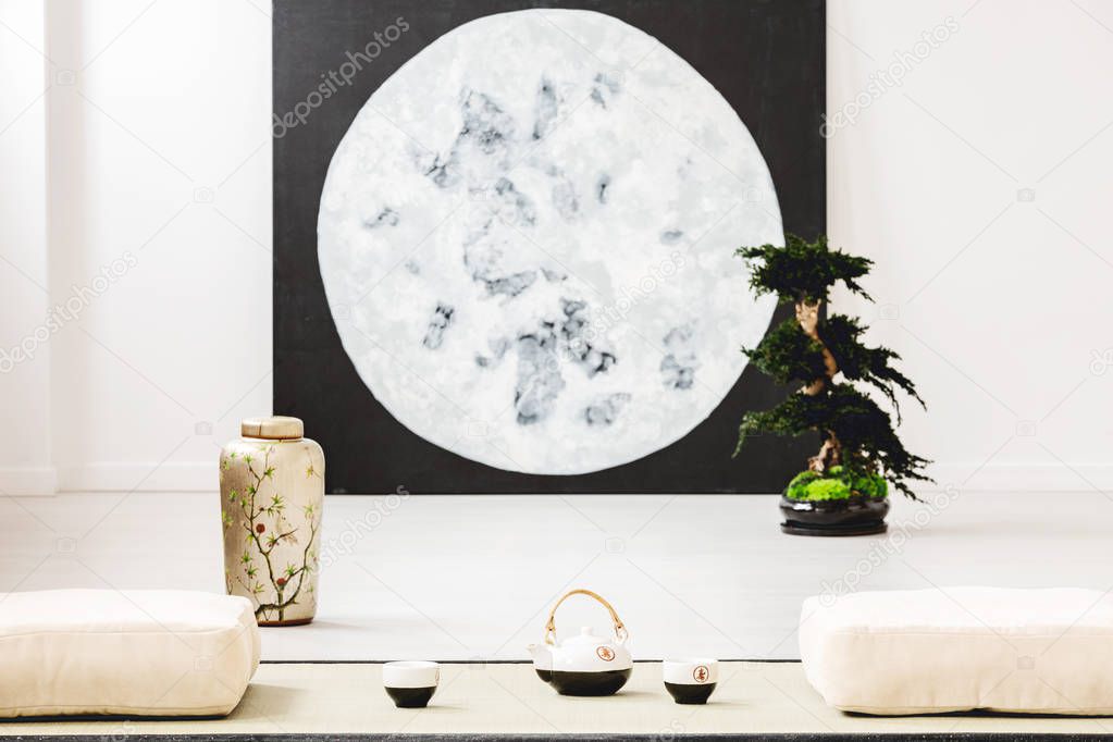 Moon poster and bonsai between pillows on the floor in japanese dining room interior. Real photo with blurred background