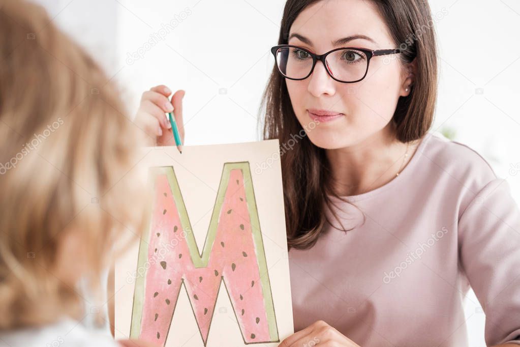 Close-up of a professional child development therapist showing a prop picture of letter 'm' to a kid during a meeting.