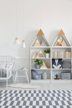 Beyaz sandalye yatak ve desenli halı ile çocuk yatak odası iç raflar arasında. Gerçek fotoğraf