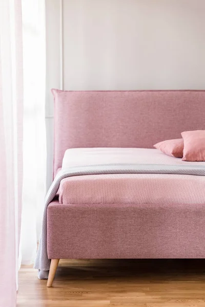 Lavender purple blanket on a pink bed with upholstered headboard in a beige bedroom interior with natural light
