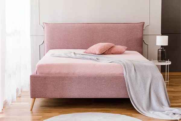 ニット ブランケットと つの枕を壁に成形と明るい寝室のインテリアに立ってパステル ピンク キングサイズ ベッドの本物の写真 — ストック写真