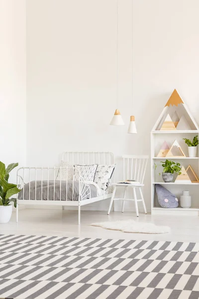 White metal bed frame with gray bedding and a checkered rug in a natural kid bedroom interior with wooden furniture and decorations