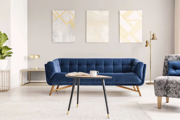 木製コーヒー テーブルな本 近代絵画 ゴールド ランプとロイヤル ブルーの長いすが明るいリビング ルーム インテリアの本物の写真でカーペットにマグカップ立って — ストック写真