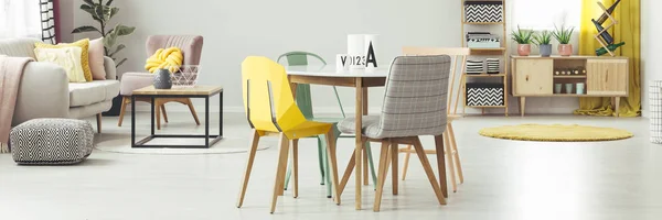 黄色和灰色的椅子在餐桌上的公寓内饰与脚凳旁边的沙发 真实照片 — 图库照片