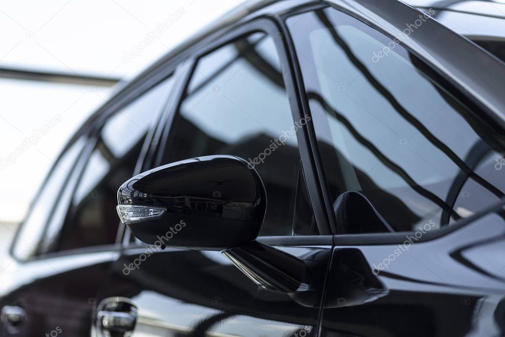 Close-up of a side mirror of a black family car for sale at a modern dealership