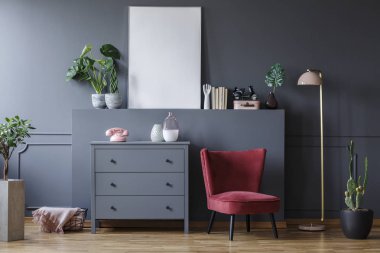 Gerçek fotoğraf kırmızı koltuk duran bir çekmeceli ve bitkiler ve süs eşyaları ile bir oturma odası iç bir ampul yanında. Boş poster grafiğiniz için bir yer ile