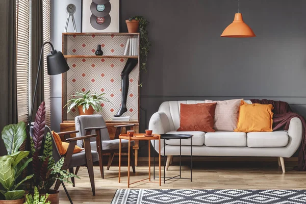 灰色の肘掛け椅子の横にある植物とビンテージのリビング ルームのインテリアのソファの上のオレンジ色のランプ — ストック写真