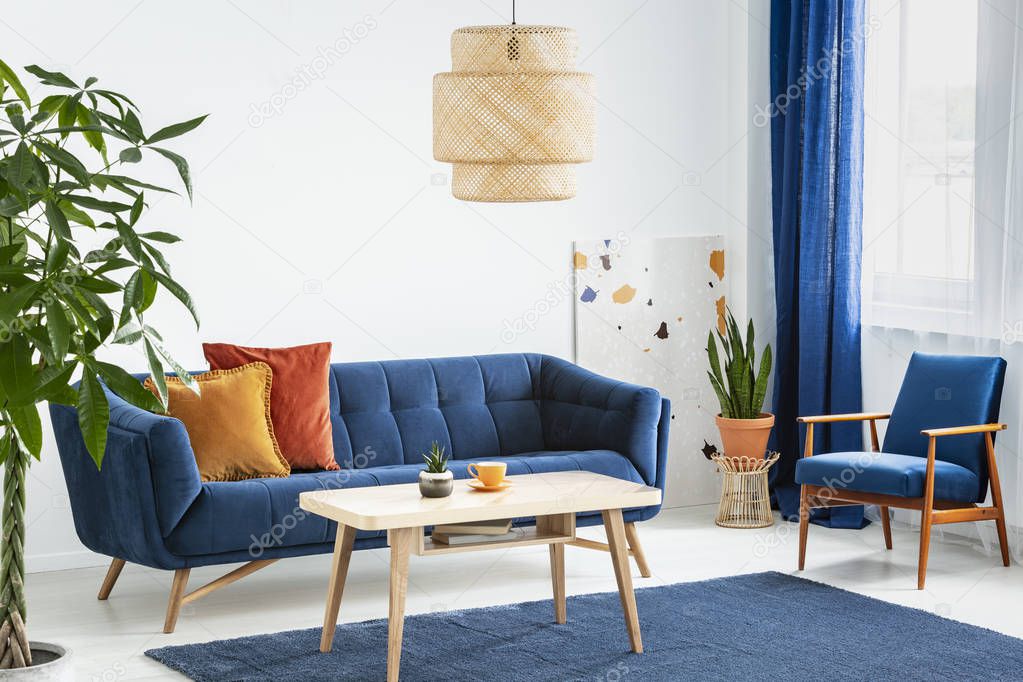 Armchair and sofa in blue and orange living room interior with lamp above wooden table. Real photo