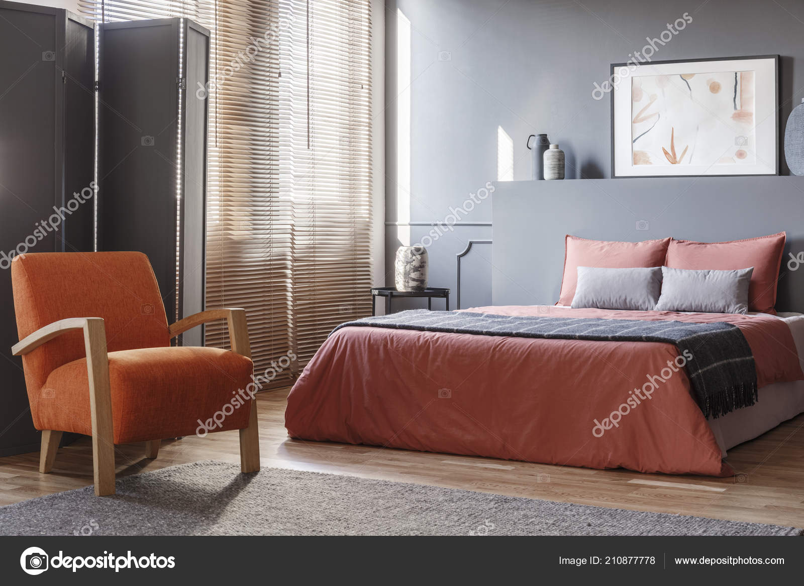 orange armchair next to pink bed in modern grey bedroom interior with  screen and poster 210877778