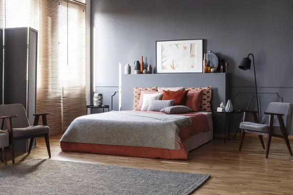 灰色木扶手椅在床旁边与红色枕头在宽敞复古卧室内部与海报 — 图库照片