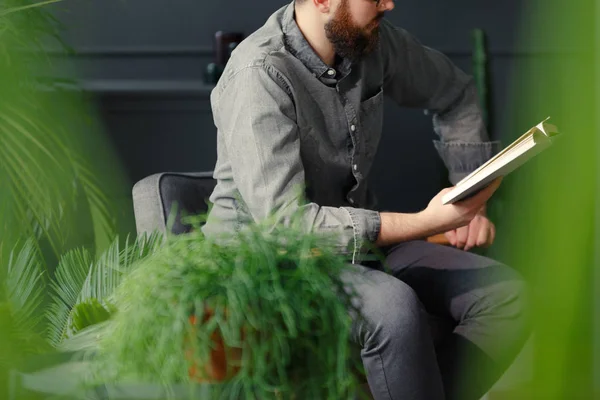 Homem Camisa Cinza Lendo Livro Enquanto Relaxa Casa Com Plantas — Fotografia de Stock
