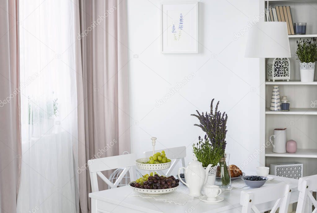 Plants on white table in bright dining room interior with poster and pink drapes at window. Real photo