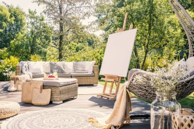 Şövale rattan masa ve koltuk yaz boyunca bahçedeki terasta mockup. Gerçek fotoğraf