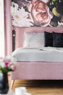 Duvardaki çiçekli siyah ve gri yastık pembe yatakta kadınsı yatak odası iç. Gerçek fotoğraf