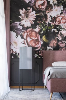 Flowers wallpaper in dark bedroom interior with black table next to pink and grey bed. Real photo clipart